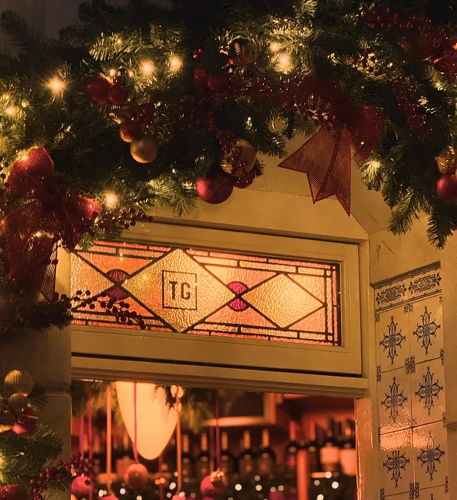 Het glas-in-loodraam met TG boven de deur, met kerstballen
